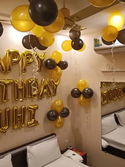 A classic and bold choice for a birthday celebration. This bedroom setup features a striking combination of black and gold balloons, with a personalized "Happy Birthday Juhi" message in large gold foil letters.