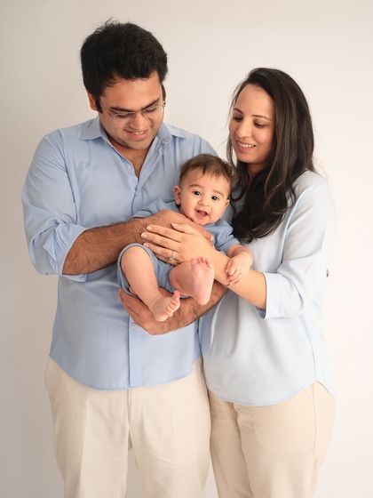 A sweet family portrait in the studio. The parents gently hold their baby, whose happy expression and bare feet add a touch of adorable realness to this classic shot.