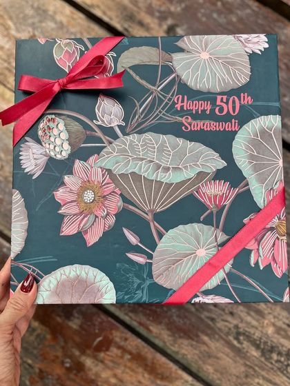 A custom-designed box for a 50th birthday, ready to be shipped from Mumbai to Chennai. The beautiful lotus-print paper and personalized name make the exterior as special as the gifts inside.