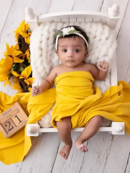 A little ray of sunshine wrapped in bright yellow. This newborn session features a pop of color with sunflowers, creating a cheerful and warm portrait on a miniature bed prop.
