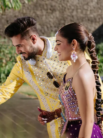 A candid shot of the bride and groom, where her long, traditional braid adds a touch of classic charm to the vibrant Mehendi celebration.