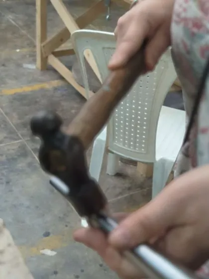 A participant carefully hammers a piece of silver, learning the precise control needed to shape metal without damaging it.