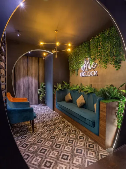 It's always 'Wine O'Clock' in this inviting reception area we designed. The space features a custom photo booth with a neon sign, lush green walls, and comfortable seating, making a great first impression.