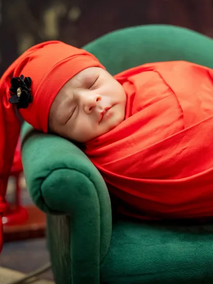 A close-up of a newborn wrapped in a vibrant red swaddle, sleeping soundly on a miniature green sofa.
