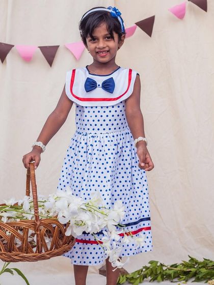 A classic look with a playful twist. This white and blue polka dot dress features a sailor-style collar and is made from breathable cotton, making it perfect for a sunny day outing.