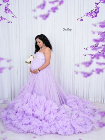 A dreamy solo portrait in a lavender ruffled gown. The floral accents and soft white background create a whimsical and ethereal look, perfect for a fairytale maternity shoot.