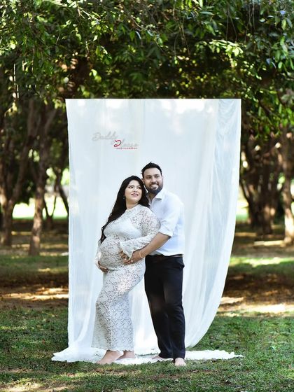 A happy couple's portrait from an outdoor session. They stand together in front of a simple white backdrop, blending the clean look of a studio with the beauty of nature.