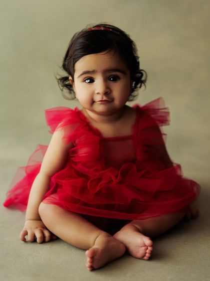 A simple, elegant portrait against a soft green backdrop, letting the baby's expression and beautiful red dress be the focus.