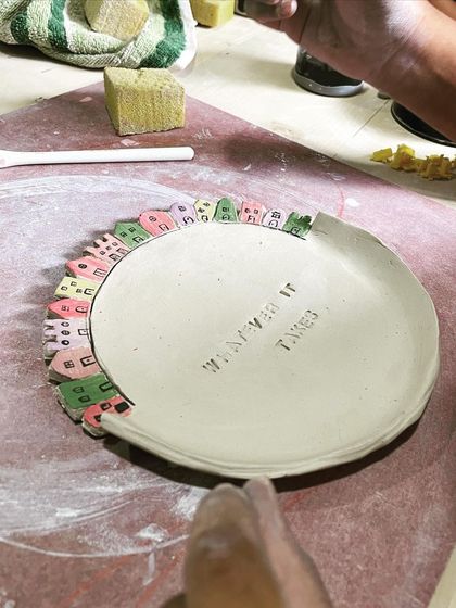 A beautifully finished plate with a border of tiny, colorful houses, showcasing a creative combination of slab building and painting.