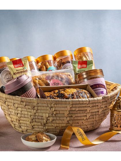 A rustic, hand-woven basket filled with a coffee mug, cake, and other treats, perfect for a cozy gift.