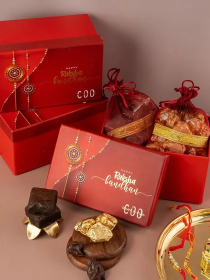 This photo captures a luxurious Raksha Bandhan gift set. We used rich red packaging and warm lighting to evoke a festive and traditional mood, highlighting the premium quality of the sweets inside.