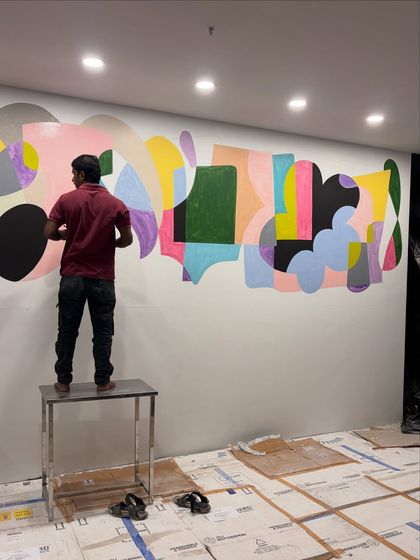 My team member working on the large-scale abstract mural. This image shows the physical effort and scale required to cover such an expansive wall with balanced, cohesive art.
