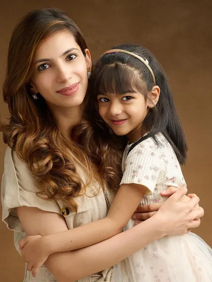 A classic mother-daughter embrace against a warm, brown painterly backdrop. The soft lighting and their close hug create a timeless and elegant portrait that feels intimate and heartfelt.