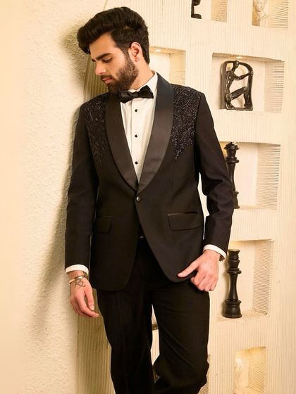 A quiet moment of reflection. This image captures the subtle luxury of a black tuxedo with embellished shoulders, a piece designed for the man who appreciates understated yet undeniable quality.