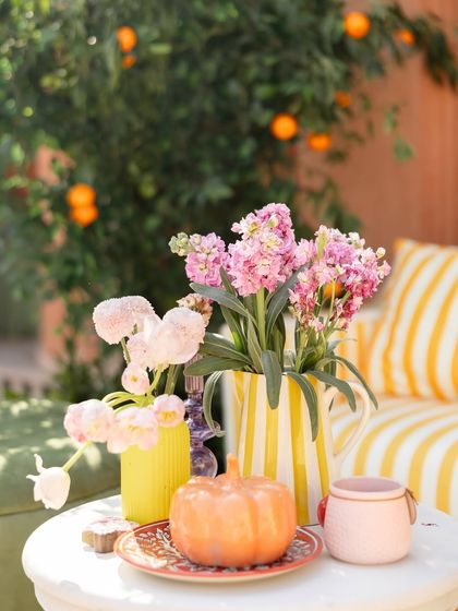 A charming tabletop detail, with a striped pitcher holding pink flowers, a ceramic pumpkin, and other colorful props.