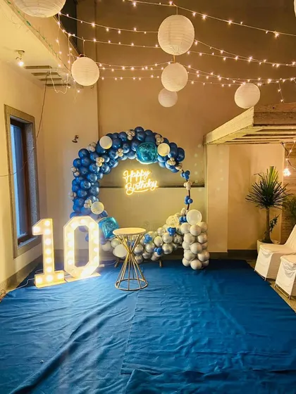 A fun and festive 10th birthday party decoration. The blue and white balloon arch, 'Happy Birthday' neon sign, and large light-up '10' create a perfect backdrop for a memorable celebration.