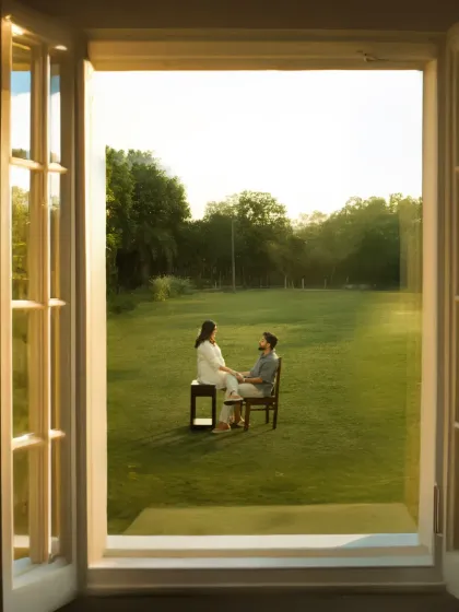A quiet conversation between two hearts, with a whole new world on the way. This unique shot captures the couple sitting together in a vast field, framed by a window, creating a sense of intimacy and anticipation.