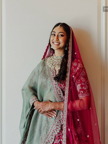 A beautiful portrait of a bride in a unique red and sage green lehenga. The makeup is kept soft and natural to balance the colors and let her youthful glow shine through.