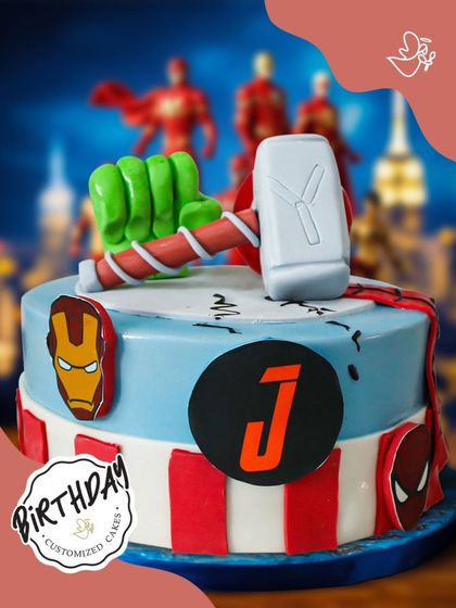 An Avengers-themed cake featuring Thor's hammer, Hulk's fist, and logos of Iron Man and Spider-Man. This personalized cake is perfect for a young Marvel fan's birthday celebration.