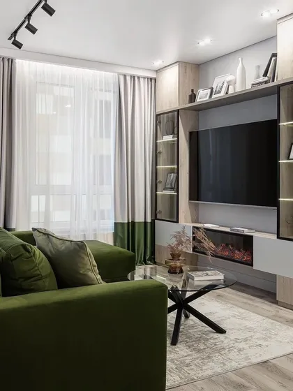 A living room with an olive green sofa and a light wood TV unit that includes an electric fireplace. The glass-door display cabinets on either side are perfect for showcasing decor.