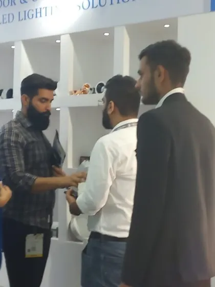A group of visitors engages with an exhibitor, learning about the latest indoor and outdoor LED lighting solutions.