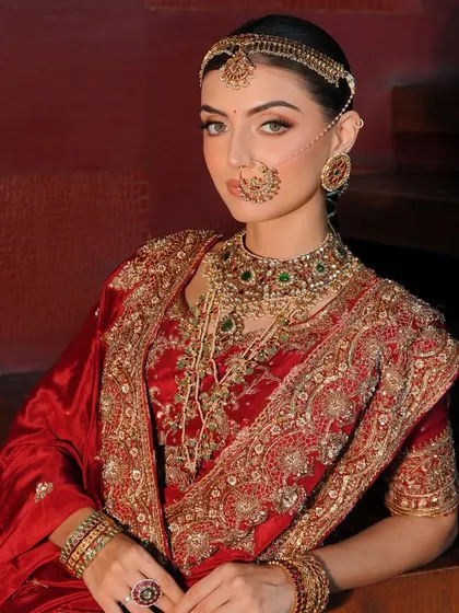 A close-up on the essence of a traditional bride. The styling focuses on the layering of jewellery, from the nath to the choker and rani haar, complementing the rich red Akriti by Shakun lehenga.