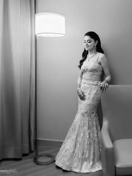 An elegant, full-length portrait of the bride in her sangeet outfit, posing gracefully by a floor lamp.