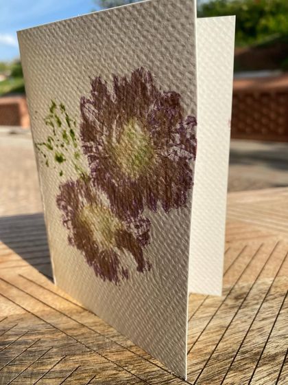 A finished greeting card with a lovely purple flower print, catching the sunlight. The texture of the watercolour paper adds another dimension to the botanical art.