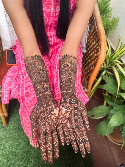 This design is rich with traditional motifs, including elephants and intricate block patterns, covering the hands and forearms in detailed artistry.