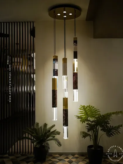 This cluster of pendant lights showcases a luxurious blend of materials, combining solid marble, fluted gold metal, and clear crystal. Suspended at varying heights, they create a dynamic and elegant focal point, ideal for stairwells or entryways.