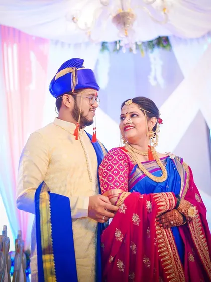A classic couple portrait from a Maharashtrian wedding. The bride and groom, in their vibrant blue and pink traditional outfits, look at each other with love and joy.
