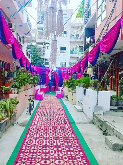 A beautiful street transformation for a Mehendi night, with pink and blue drapes, carpets, and lighting creating an enchanting pathway.