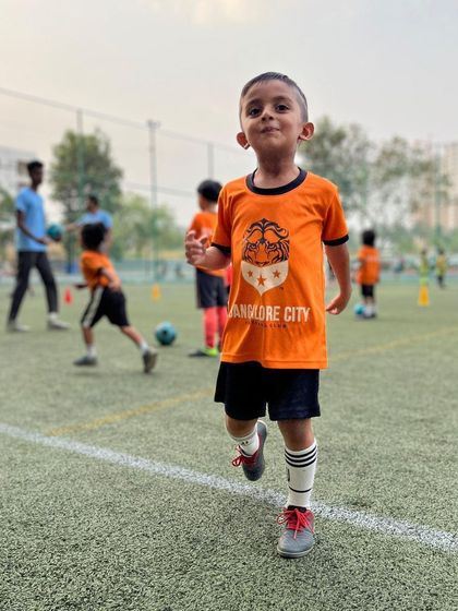The pure joy of football. A young player from our grassroots program runs on the pitch with a huge smile, embodying the fun-first environment we create.