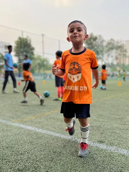 The pure joy of football. A young player from our grassroots program runs on the pitch with a huge smile, embodying the fun-first environment we create.