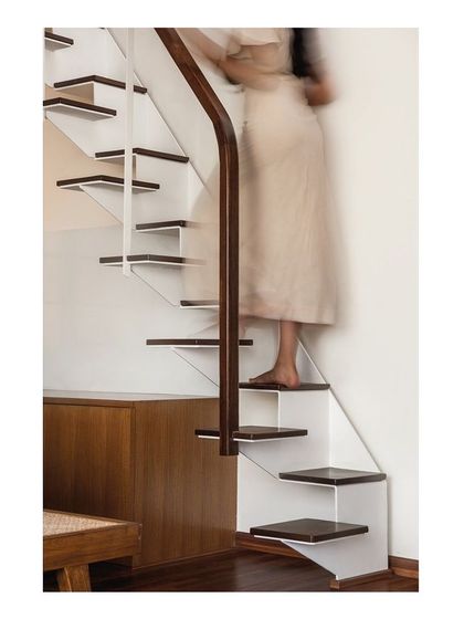 Detail of a secondary staircase, designed with folded white steel plates and dark wood treads. This compact, alternating tread stair is a functional sculpture, providing access to a loft space while occupying a minimal footprint.