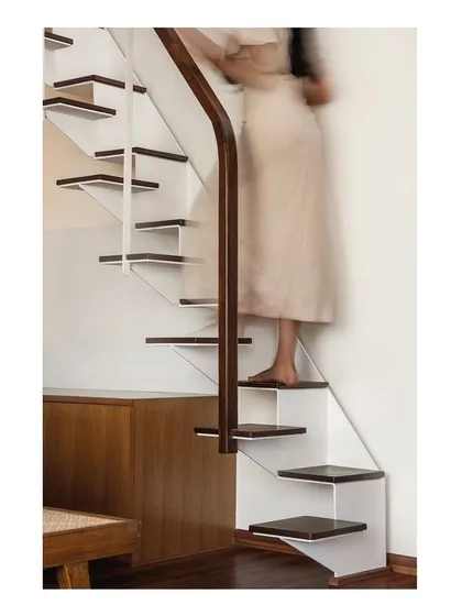 Detail of a secondary staircase, designed with folded white steel plates and dark wood treads. This compact, alternating tread stair is a functional sculpture, providing access to a loft space while occupying a minimal footprint.