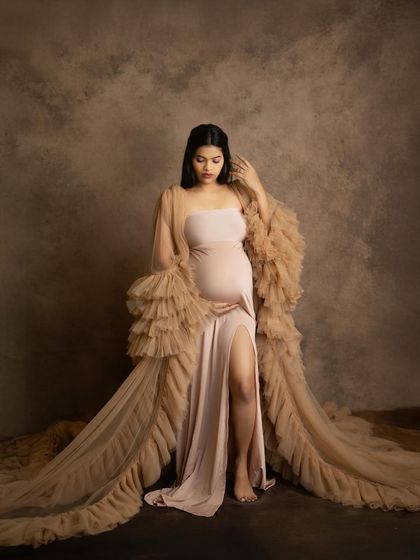 The combination of a fitted gown and a dramatic ruffled robe adds texture and glamour to this studio portrait. It’s a look that makes any mom-to-be feel incredibly special.