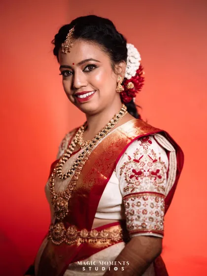 A stunning studio-style portrait of the bride against a vibrant red background. This makes her traditional white saree and gold jewelry pop.
