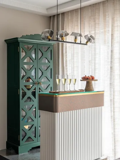 A chic and modern home bar setup perfect for entertaining. The fluted white bar counter is complemented by a vintage-style green cabinet, creating a beautiful mix of contemporary and classic design.