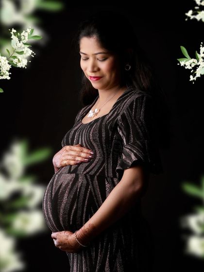 A beautiful solo portrait in a sparkling black gown, framed by soft white flowers. The dark background makes the dress and the mother's serene expression stand out.
