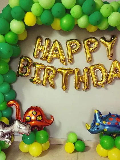 A creative Dinosaur-themed birthday setup at home, using a green balloon half-arch and large dinosaur foil balloons.