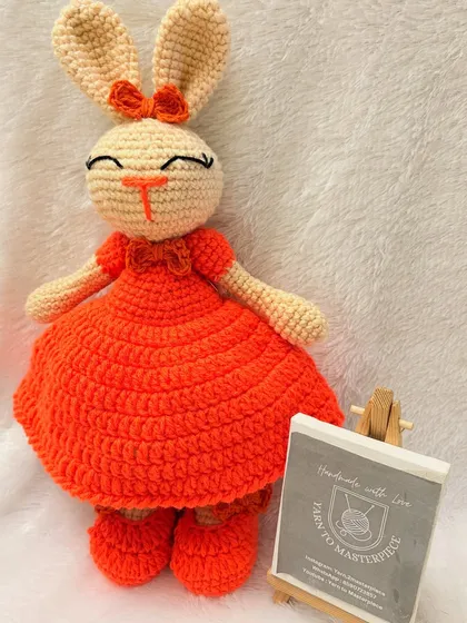 This cheerful 14-inch bunny is one of my most loved creations. Dressed in a bright orange frock with a matching bow, she is handmade with durable cotton yarn, making her a perfect, huggable friend for children.