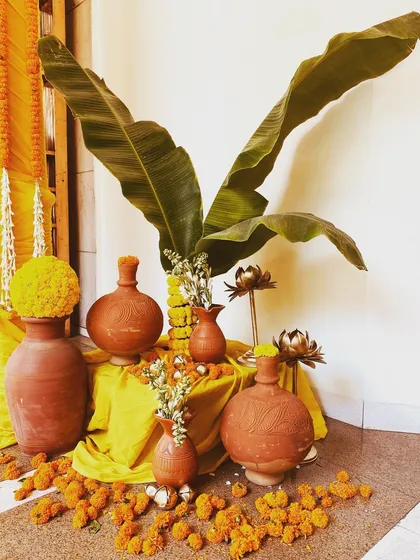 A rustic decor detail for a South Indian themed event. Earthen matkas and fresh banana leaves are artfully arranged with scattered marigold flowers, creating an authentic and earthy aesthetic.