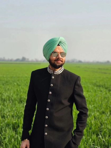 A stunning shot of Jaspreet Singh in the black sherwani against a field of green, blending modern fashion with nature.