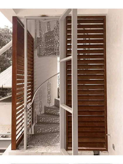A spiral staircase with intricately cut steps, viewed through a wooden louvered door, showcasing our attention to detailed metal and woodwork.