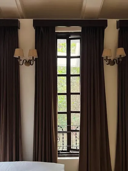 I love the grandeur of these tall, dark-framed windows. Paired with classic wall sconces and heavy drapes, they create a sense of drama and luxury, flooding the room with light while framing the view beautifully.
