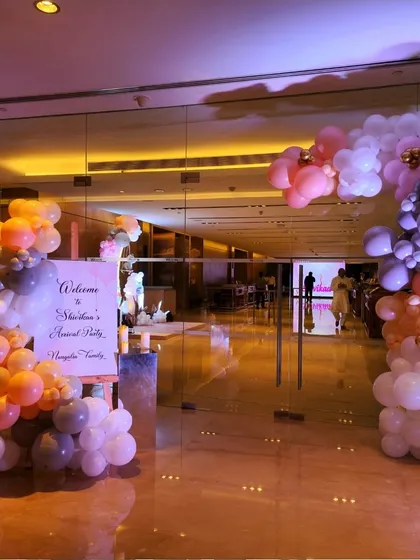 A whimsical balloon arch in pastel shades of orange, grey, and white welcomes guests to a baby's arrival party. The design is modern, soft, and celebratory.