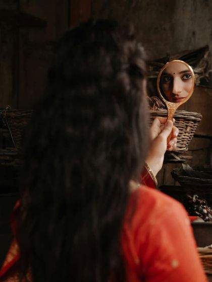 A creative and mysterious shot, capturing the model's reflection in a traditional handheld mirror against a rustic, dark background.