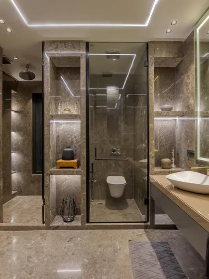This master bathroom design is all about creating a spa-like experience, with extensive use of warm-toned marble, a floating vanity, and multiple illuminated niches for storage and ambiance.