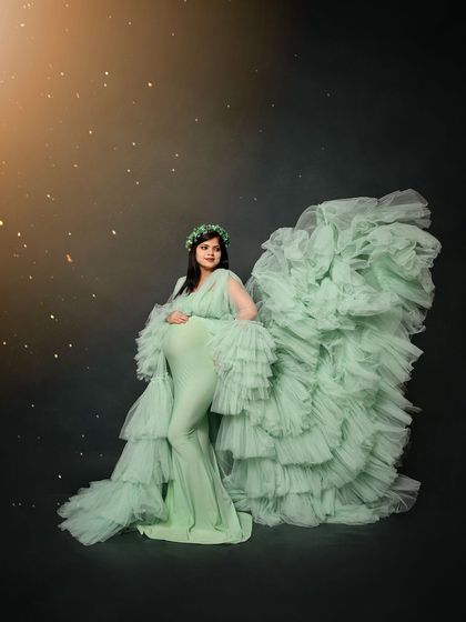 A dramatic solo portrait of the mom-to-be in a mint green ruffled gown. The dark, moody background with subtle sparkles makes the gown appear to glow.